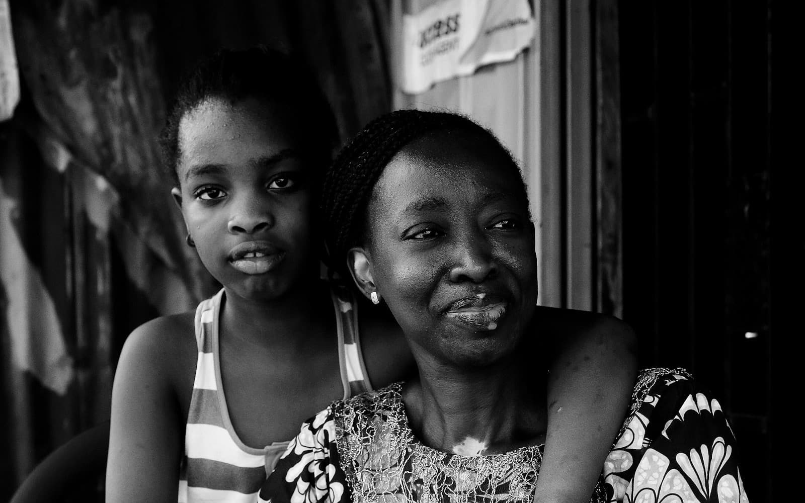 Black and white portrait of a smiling mother with her daughter's arm around her shoulders.